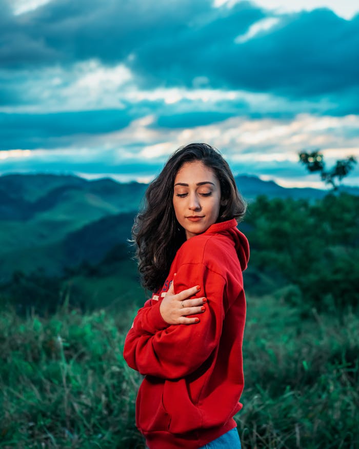 gallery-06 Serene woman in red hoodie enjoying nature with mountains in the background.