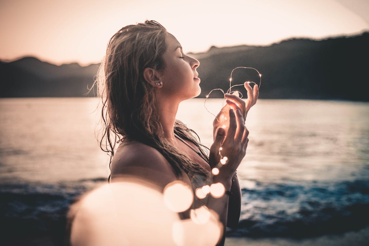 A woman enjoys a serene sunset on a beach in Ubatuba, Brazil holding glowing lights.